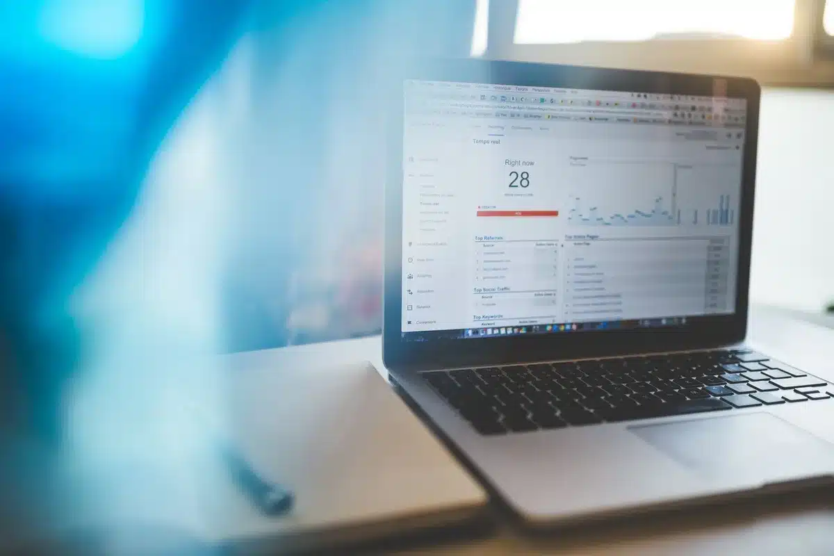 A bright desk with an open laptop showing a generic analytics dashboard, not readable, beside a notebook and pen