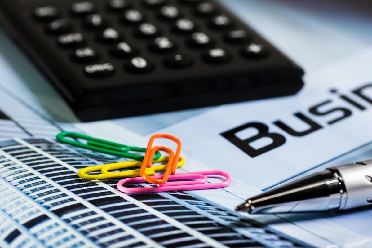 A well-lit desk with a printed accounting ledger open, a pen resting on a dated line and a calculator nearby