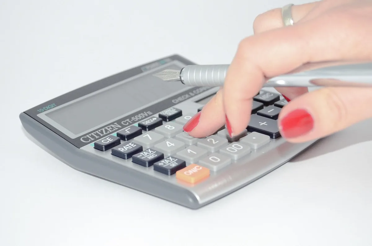 clean desk with calculator, printed tax forms, and hands writing numbers