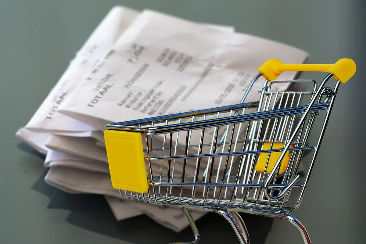 hands sorting receipts on a wooden desk next to a laptop showing a budgeting spreadsheet