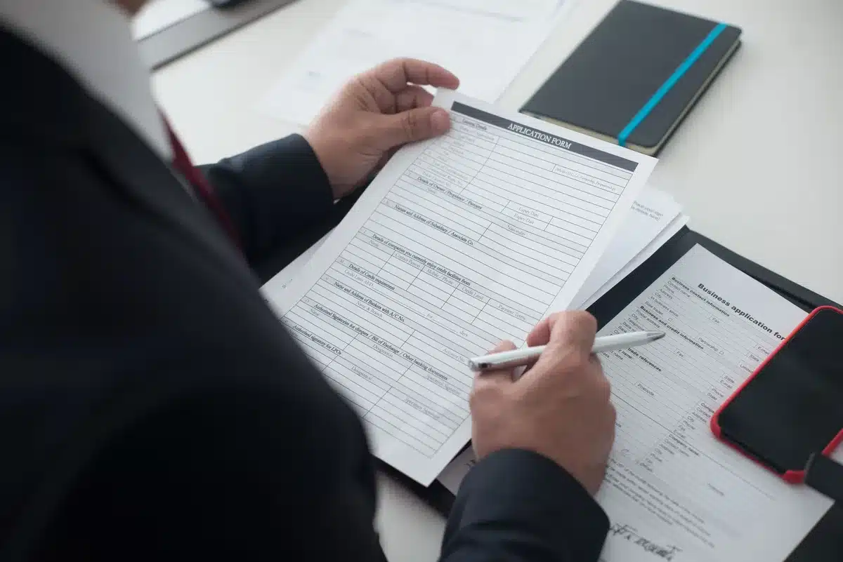 A tidy desk with hands filling a company-formation form, a laptop open to a registration page, a notepad and pen nearby